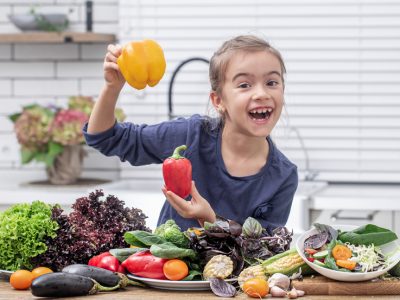 menina sorrindo segurando pimentão rodeada por alimentos saudáveis