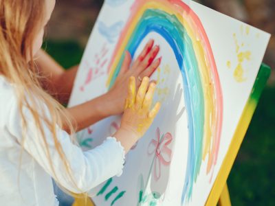 Criança pintando um arco-íris com as mãos.