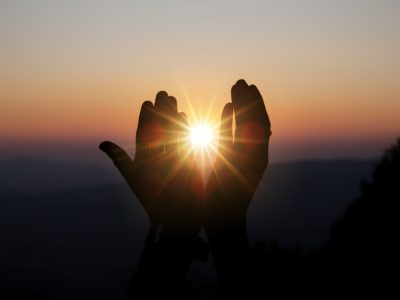 Mãos emoldurando o sol durante o pôr do sol, simbolizando paz.