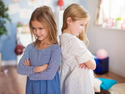 Duas meninas brigando, de braços cruzados e costas viradas.